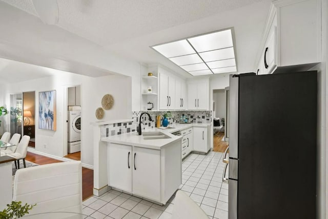 kitchen with sink, stainless steel fridge, backsplash, white cabinets, and washer / dryer