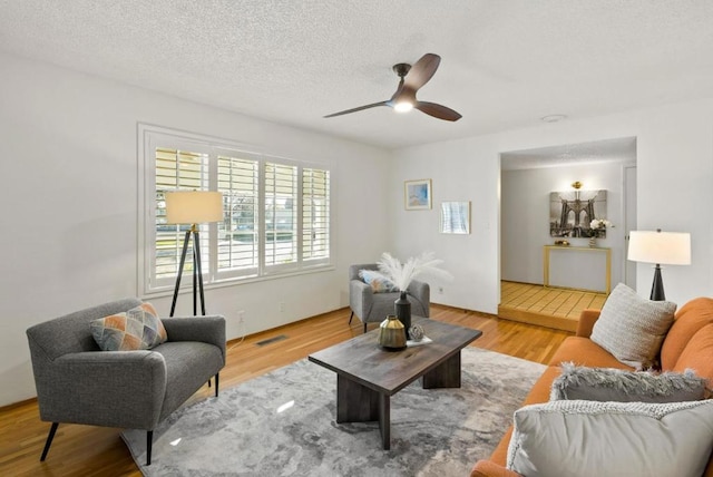 living room with hardwood / wood-style flooring, ceiling fan, and a textured ceiling