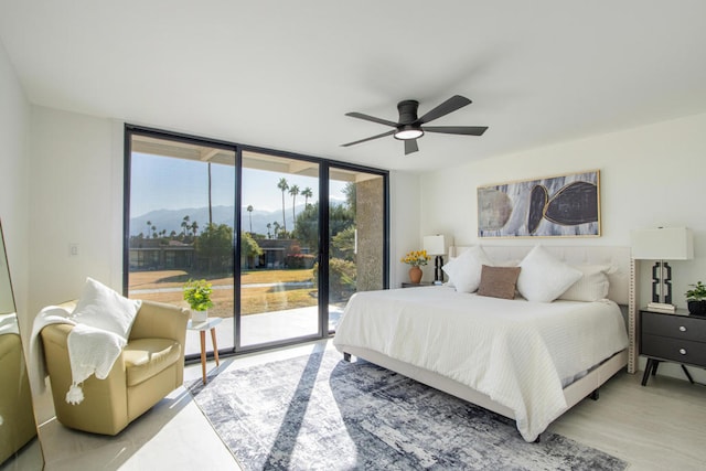 bedroom with expansive windows, access to exterior, ceiling fan, a mountain view, and light wood-type flooring