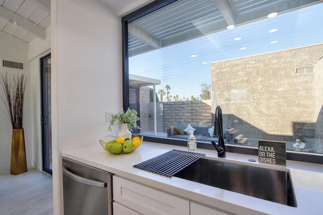 kitchen featuring beamed ceiling, stainless steel dishwasher, sink, and white cabinets