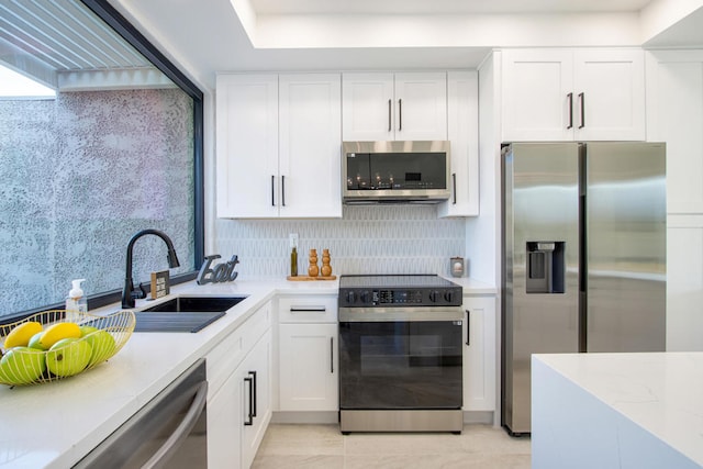 kitchen featuring appliances with stainless steel finishes, sink, white cabinets, backsplash, and light stone counters