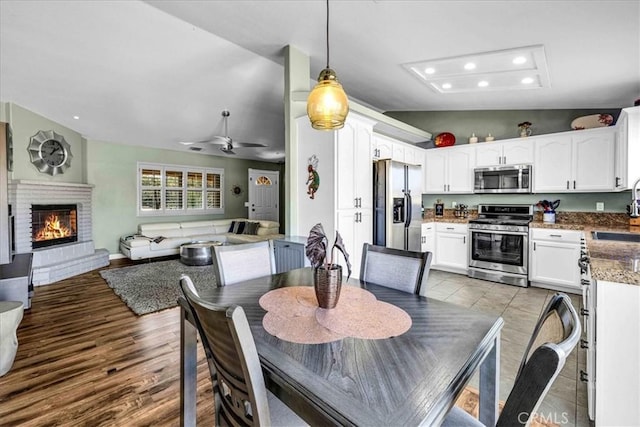 dining area with sink, a fireplace, ceiling fan, and light wood-type flooring