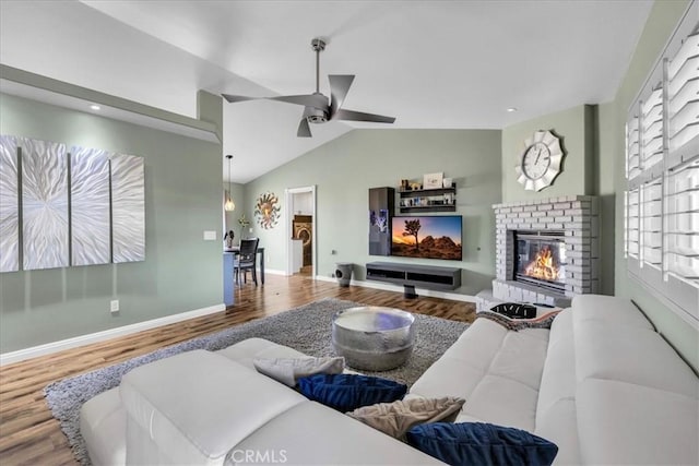 living room with ceiling fan, lofted ceiling, hardwood / wood-style floors, and a brick fireplace