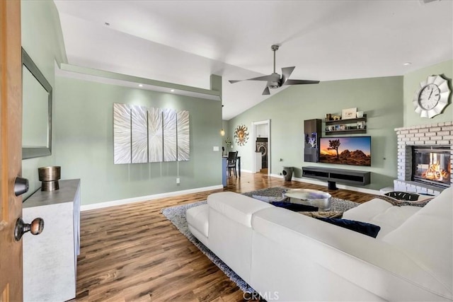 living room featuring ceiling fan, a fireplace, wood-type flooring, and vaulted ceiling