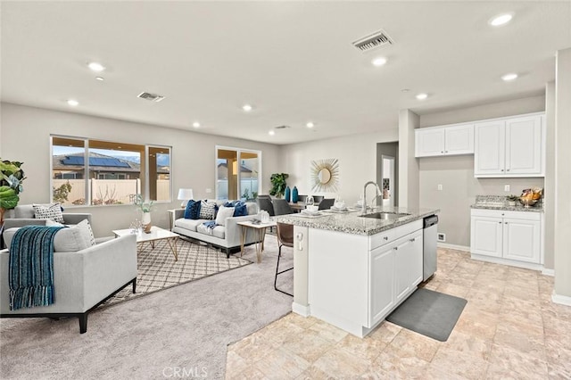 kitchen with dishwasher, white cabinetry, sink, an island with sink, and light stone countertops