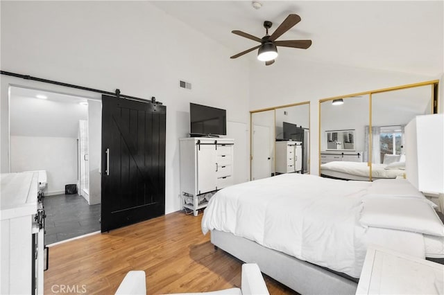 bedroom featuring hardwood / wood-style floors, high vaulted ceiling, ceiling fan, multiple closets, and a barn door