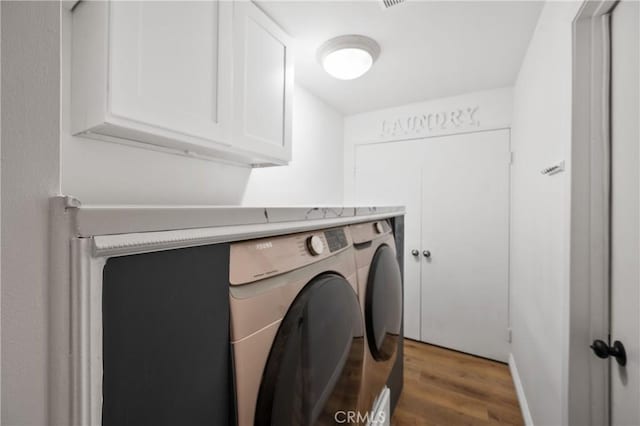 clothes washing area with cabinets, wood-type flooring, and washing machine and clothes dryer