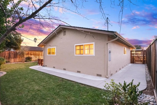 property exterior at dusk featuring a yard and a patio area