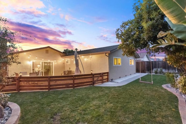 back house at dusk featuring a lawn