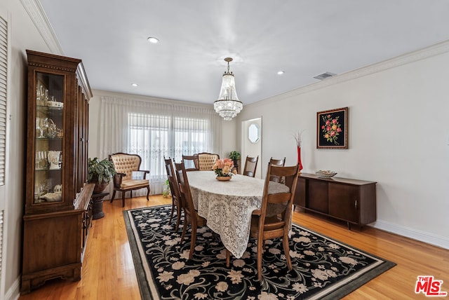 dining area with crown molding, an inviting chandelier, and light hardwood / wood-style flooring