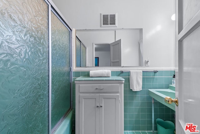 bathroom with tile walls and shower / bath combination with glass door