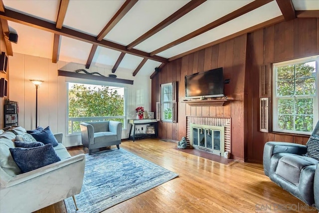 living room with light hardwood / wood-style flooring, a fireplace, wooden walls, and lofted ceiling with beams