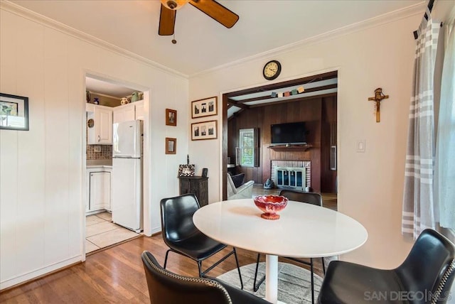 dining room with crown molding, ceiling fan, a fireplace, and light hardwood / wood-style flooring