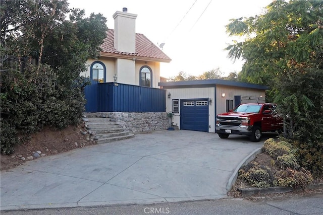 view of front of home with a chimney, concrete driveway, an outdoor structure, a garage, and a tiled roof