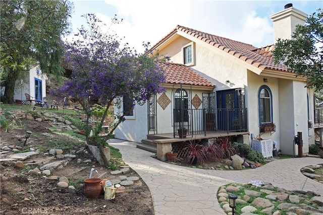 mediterranean / spanish house with a chimney, stucco siding, and a tile roof