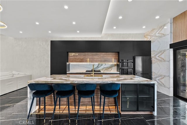 kitchen featuring a large island, a breakfast bar area, light stone countertops, and stainless steel refrigerator