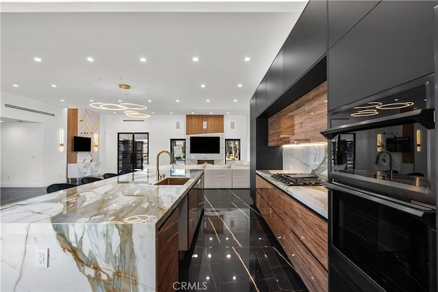 kitchen featuring sink, hanging light fixtures, a barn door, stainless steel gas cooktop, and light stone countertops