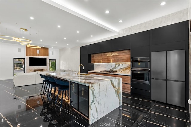 kitchen with sink, hanging light fixtures, a spacious island, light stone counters, and a kitchen bar