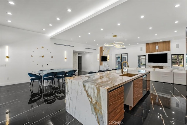 kitchen with light stone counters, sink, and a large island with sink