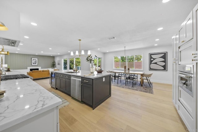 kitchen featuring stainless steel appliances, light stone countertops, light hardwood / wood-style floors, white cabinets, and decorative light fixtures