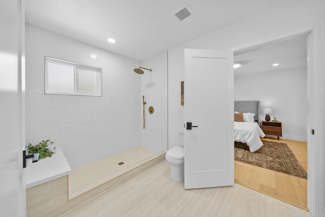 bathroom with hardwood / wood-style flooring, toilet, and a tile shower