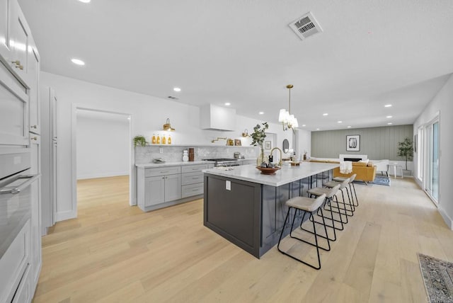 kitchen featuring a breakfast bar area, hanging light fixtures, an island with sink, light hardwood / wood-style floors, and backsplash