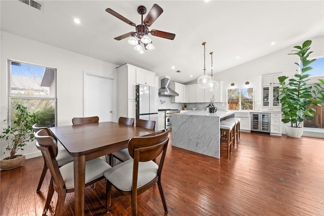 dining area with ceiling fan, beverage cooler, dark hardwood / wood-style flooring, and vaulted ceiling