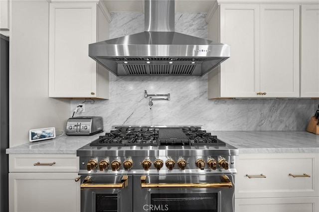 kitchen featuring double oven range, white cabinets, light stone counters, and wall chimney exhaust hood