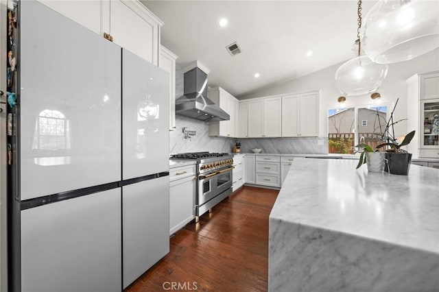 kitchen with wall chimney range hood, white cabinetry, white refrigerator, light stone countertops, and range with two ovens