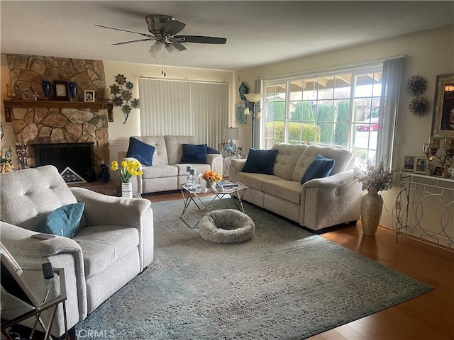 living room with hardwood / wood-style floors, a stone fireplace, and ceiling fan