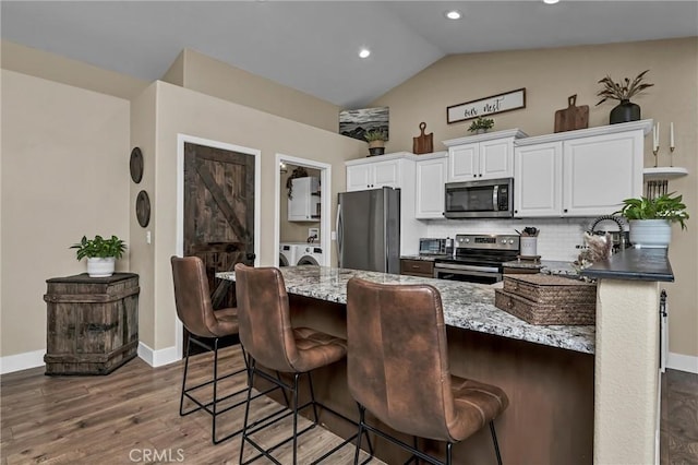 kitchen featuring a kitchen bar, white cabinetry, separate washer and dryer, vaulted ceiling, and stainless steel appliances