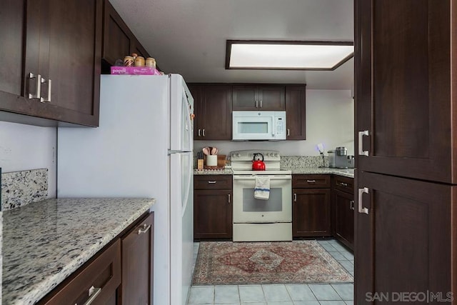 kitchen with light tile patterned flooring, light stone countertops, dark brown cabinets, and white appliances