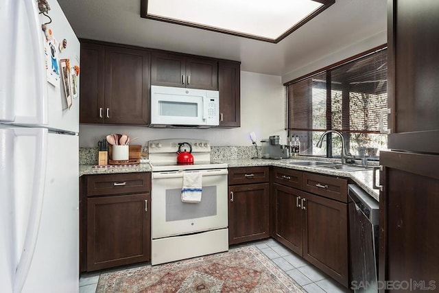 kitchen with sink, white appliances, light tile patterned floors, dark brown cabinetry, and light stone countertops