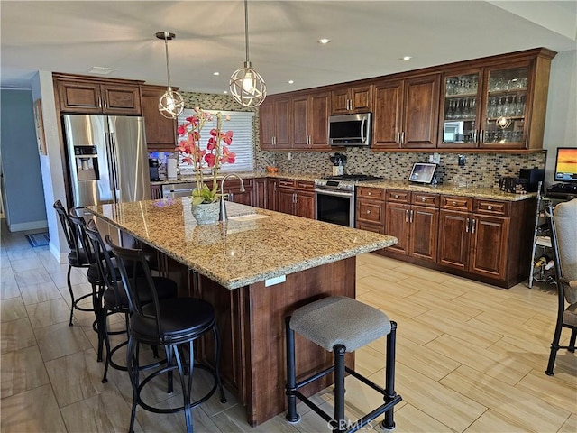 kitchen featuring sink, stainless steel appliances, an island with sink, a kitchen bar, and decorative light fixtures