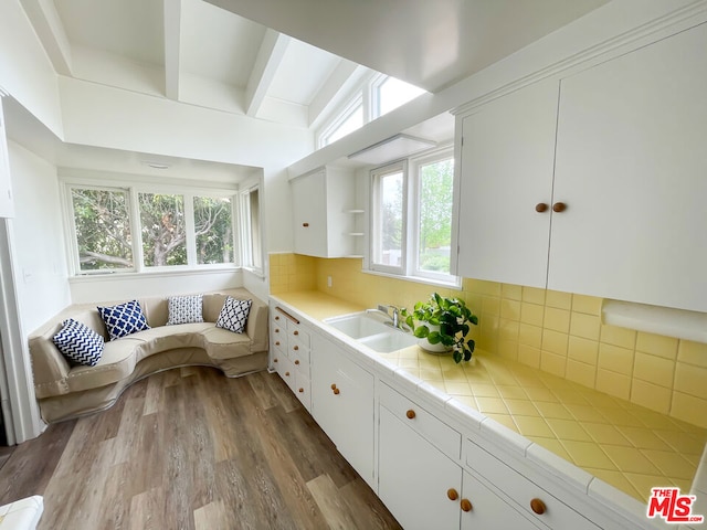 kitchen with sink, backsplash, light hardwood / wood-style floors, white cabinets, and tile countertops