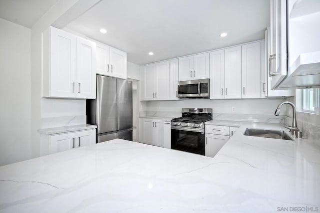 kitchen with light stone counters, white cabinetry, appliances with stainless steel finishes, and sink