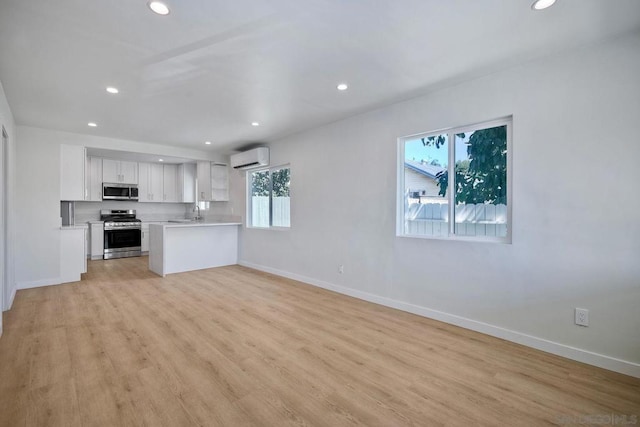 kitchen featuring appliances with stainless steel finishes, white cabinetry, sink, a wall unit AC, and light hardwood / wood-style flooring