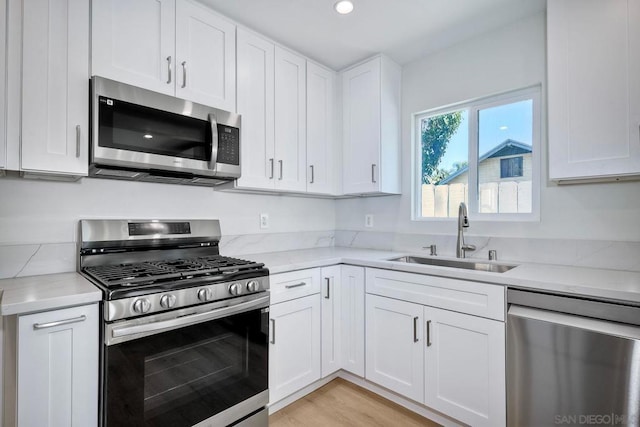 kitchen featuring sink, stainless steel appliances, light stone counters, white cabinets, and light wood-type flooring