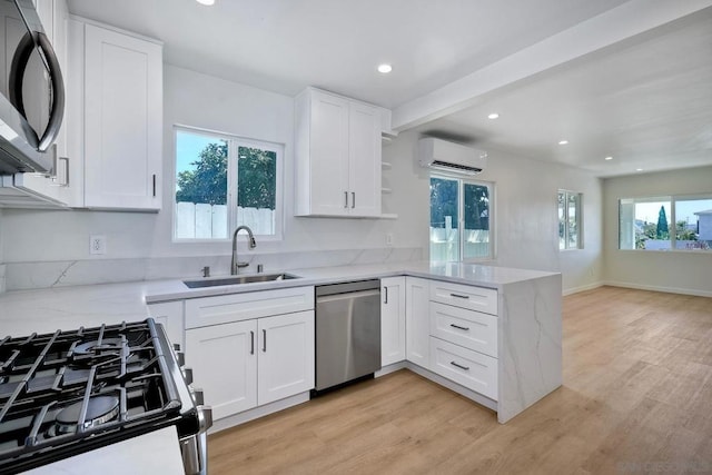 kitchen featuring sink, appliances with stainless steel finishes, white cabinetry, a wall mounted air conditioner, and light wood-type flooring