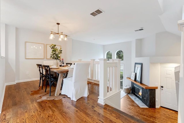 dining area featuring a tile fireplace, vaulted ceiling, hardwood / wood-style floors, and a notable chandelier