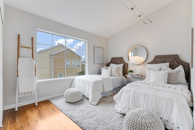 bedroom featuring wood-type flooring, vaulted ceiling, and rail lighting