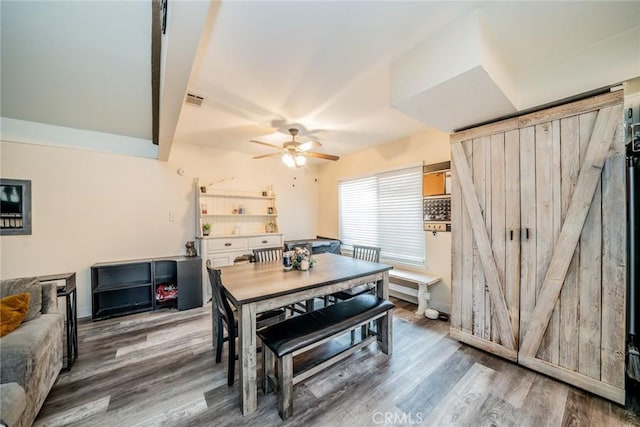 dining room with wood-type flooring, a barn door, and ceiling fan