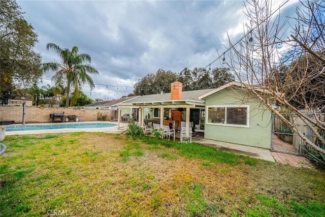 rear view of house with a fenced in pool, a patio area, and a lawn