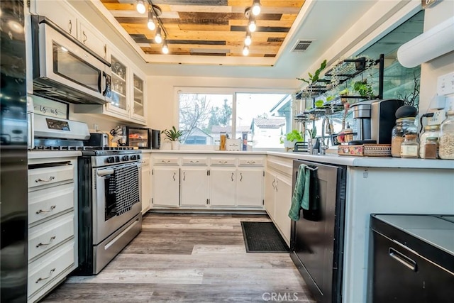 kitchen with light hardwood / wood-style flooring, stainless steel appliances, track lighting, white cabinets, and a raised ceiling