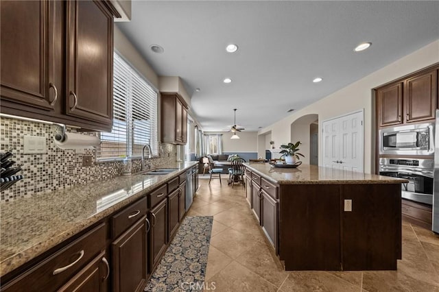 kitchen with a kitchen island, sink, decorative backsplash, stainless steel appliances, and light stone countertops