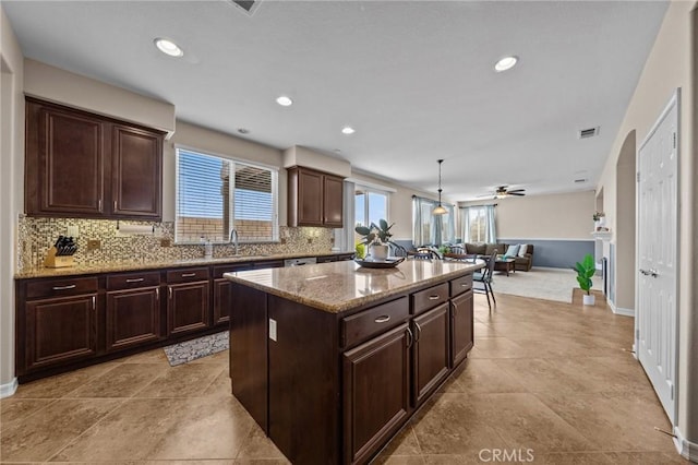 kitchen with pendant lighting, sink, light stone counters, tasteful backsplash, and a kitchen island