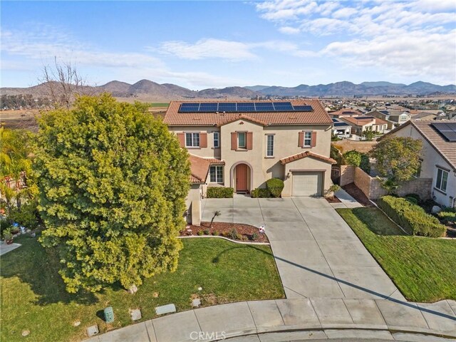 mediterranean / spanish-style house with a garage, a mountain view, a front lawn, and solar panels