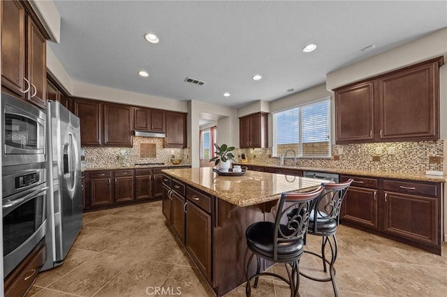 kitchen with dark brown cabinetry, a kitchen breakfast bar, appliances with stainless steel finishes, and a kitchen island