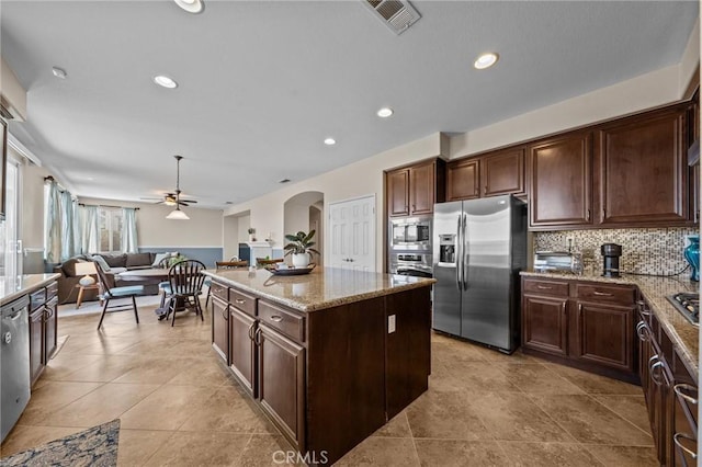 kitchen with backsplash, dark brown cabinets, stainless steel appliances, light stone countertops, and a kitchen island