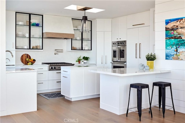 kitchen with white cabinetry, hanging light fixtures, light hardwood / wood-style floors, and appliances with stainless steel finishes